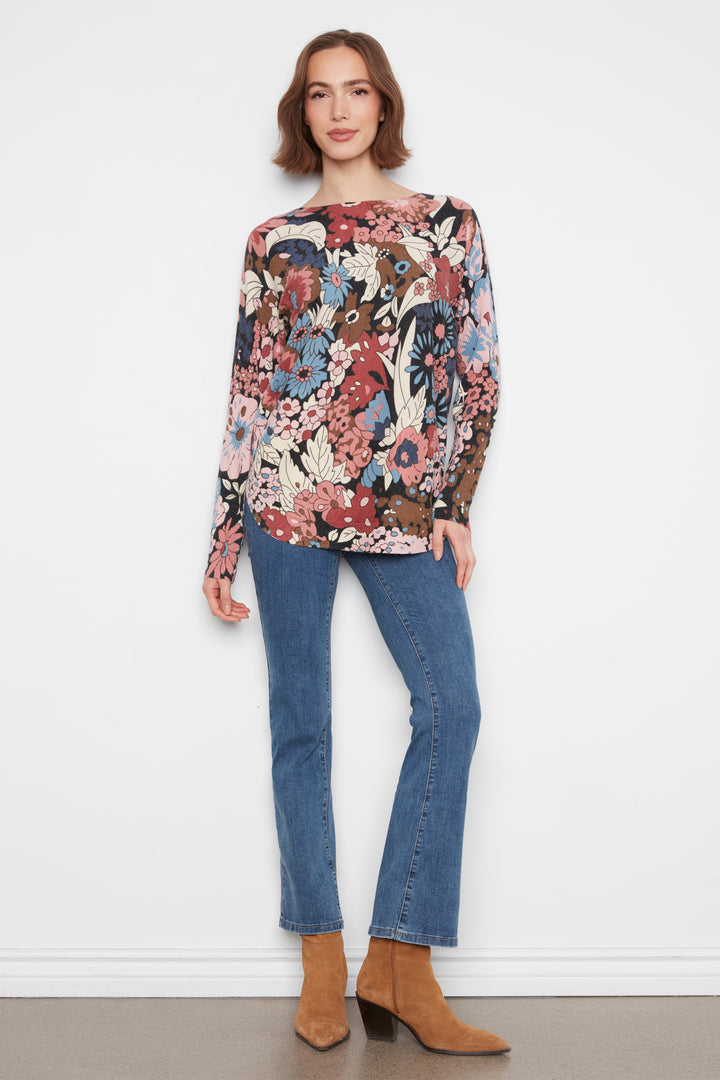 A woman wearing a long sleeve flower print sweater top standing in front of a white wall. 
