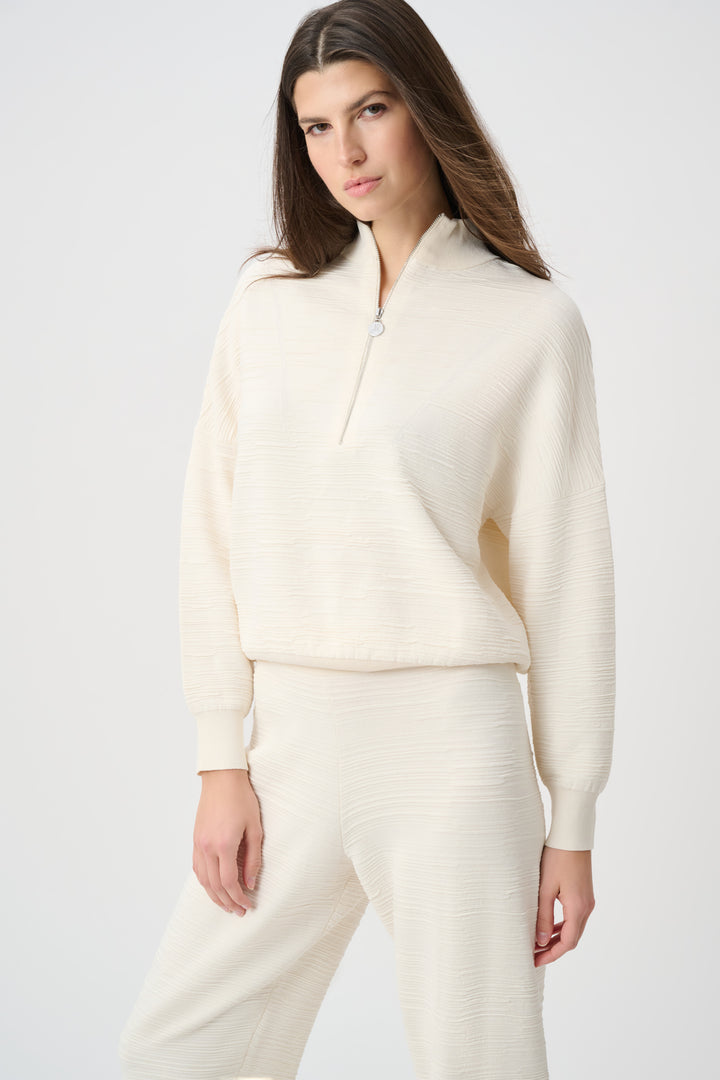 A woman wearing a cream half-zip textured sweatshirt with matching pants standing in front of a white background. 