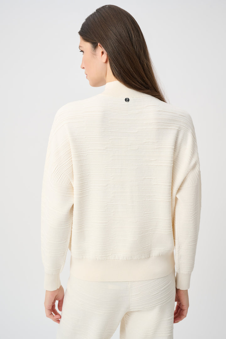 A woman shown from the back wearing a cream half-zip textured sweatshirt with matching pants standing in front of a white background. 