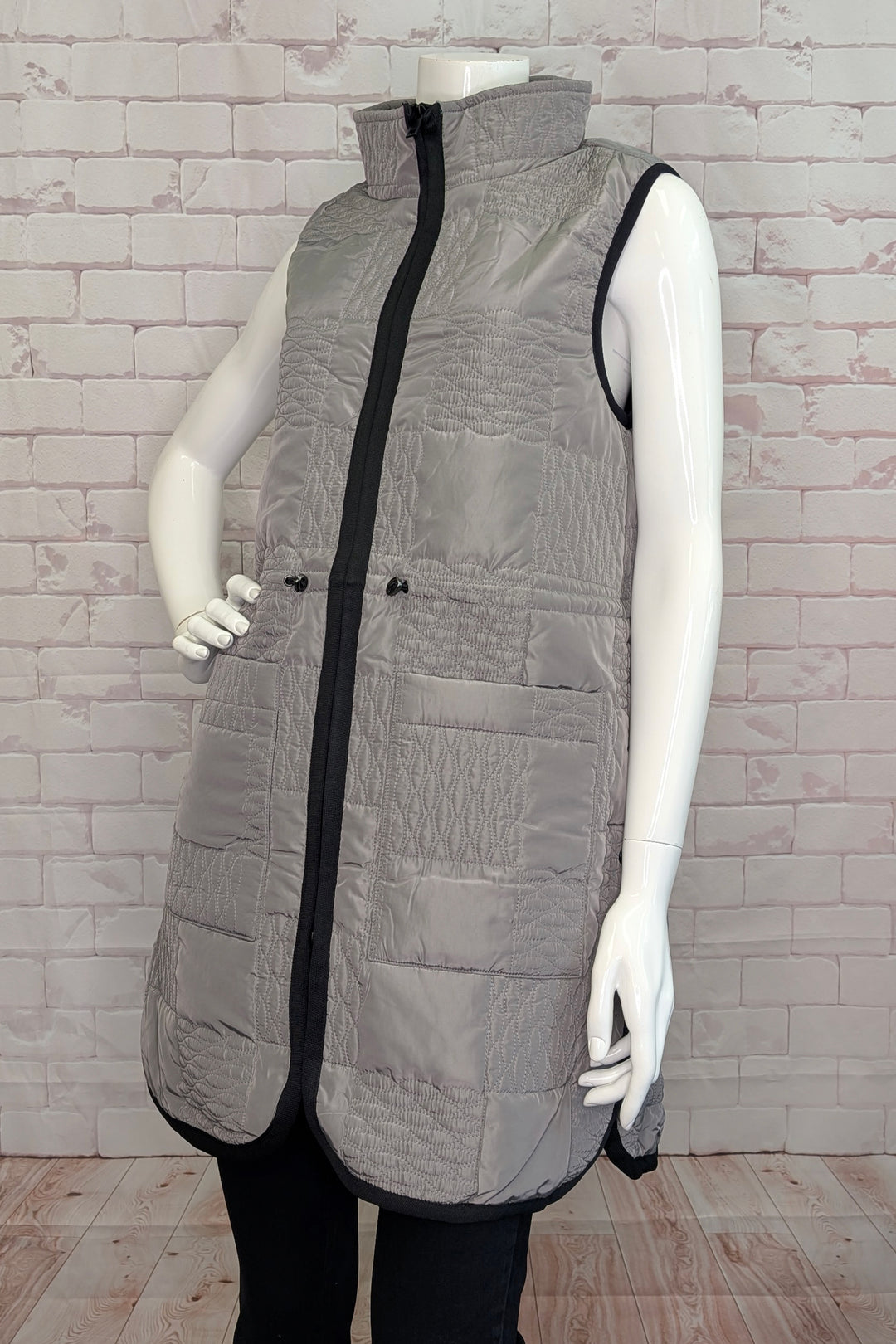 Gray quilted vest on a mannequin against a light brick wall.