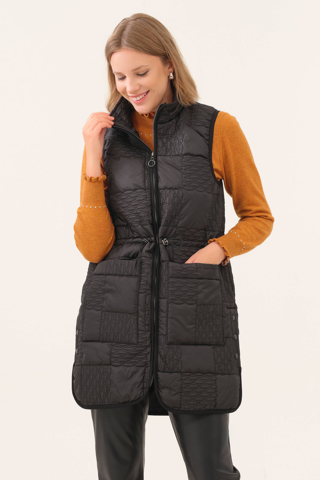 Woman wearing a black puffer vest over a mustard yellow long-sleeve shirt on a beige background