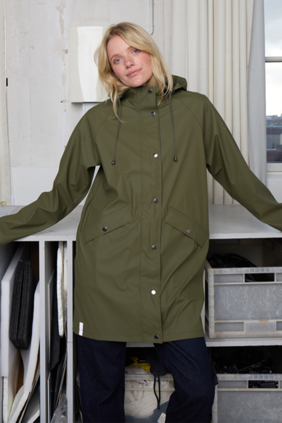 Person wearing a green raincoat standing indoors.