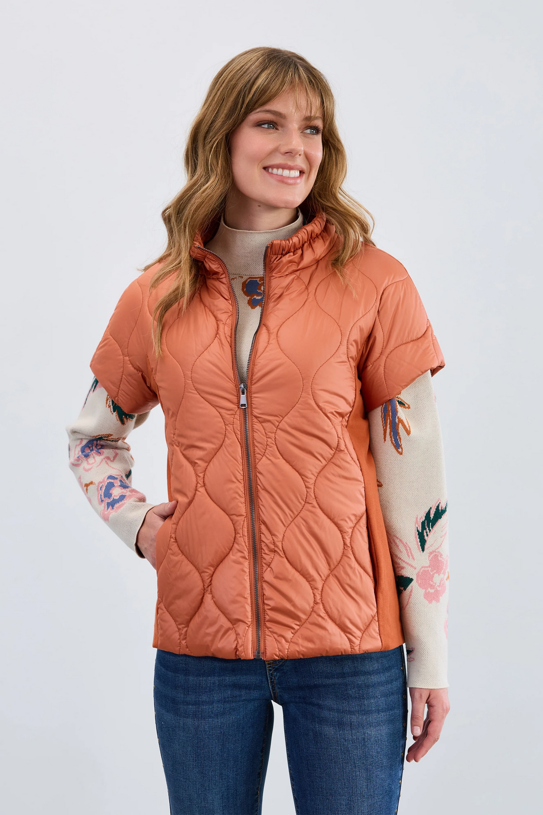Woman wearing a quilted orange jacket with floral sleeves on a white background