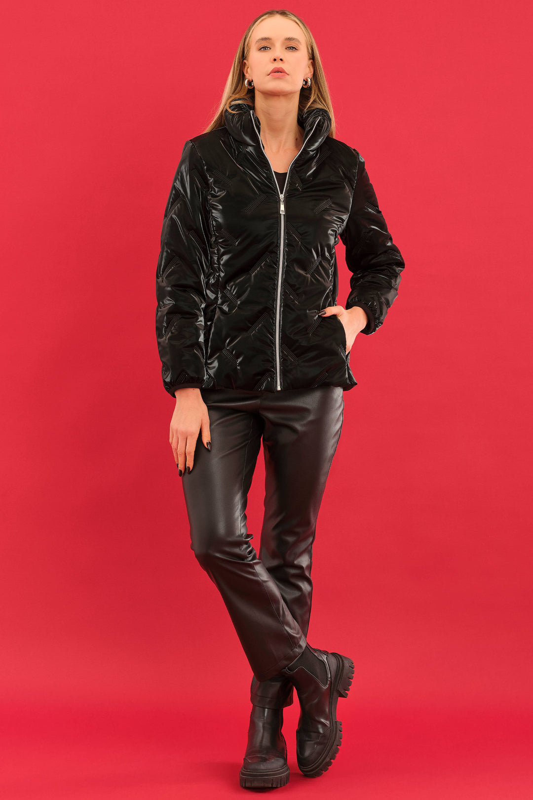 Woman wearing a black shiny puffer jacket, pants, and boots on a red background