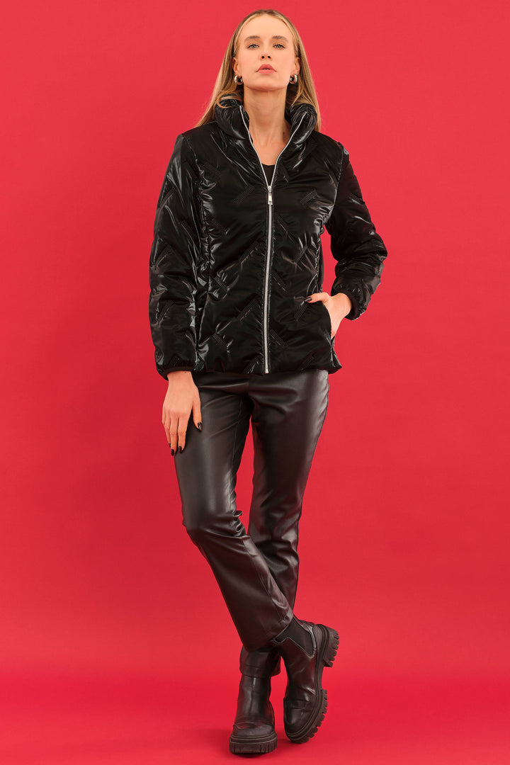 Woman wearing a black shiny puffer jacket, pants, and boots on a red background