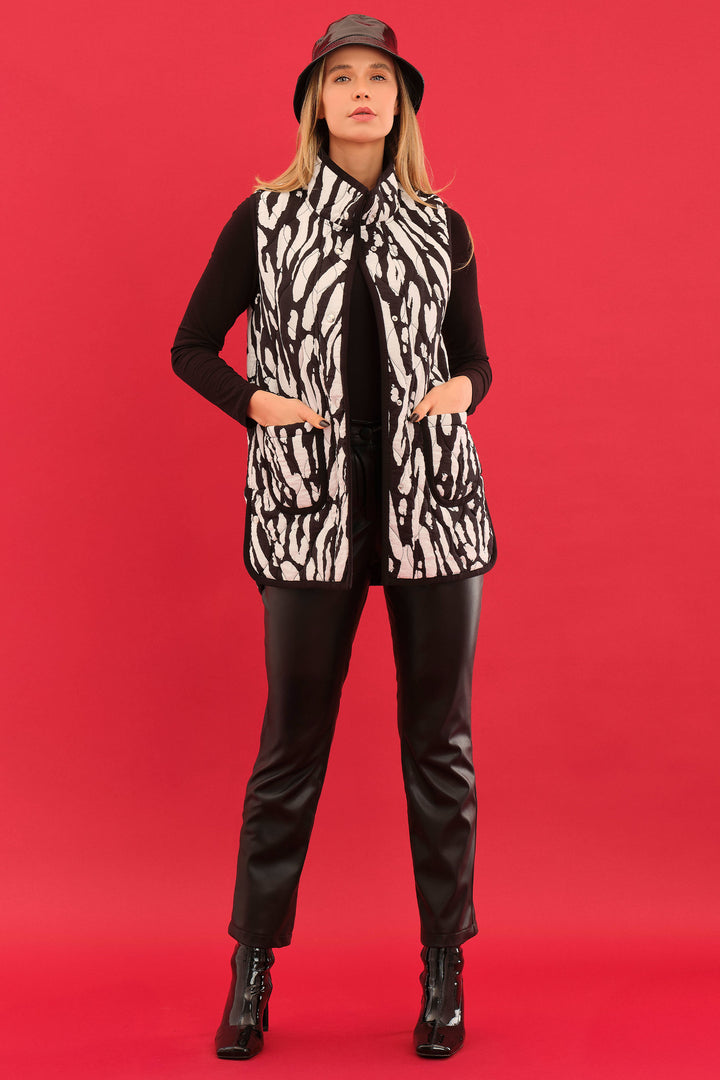 Woman wearing a zebra print vest, black top, pants, and hat on a red background