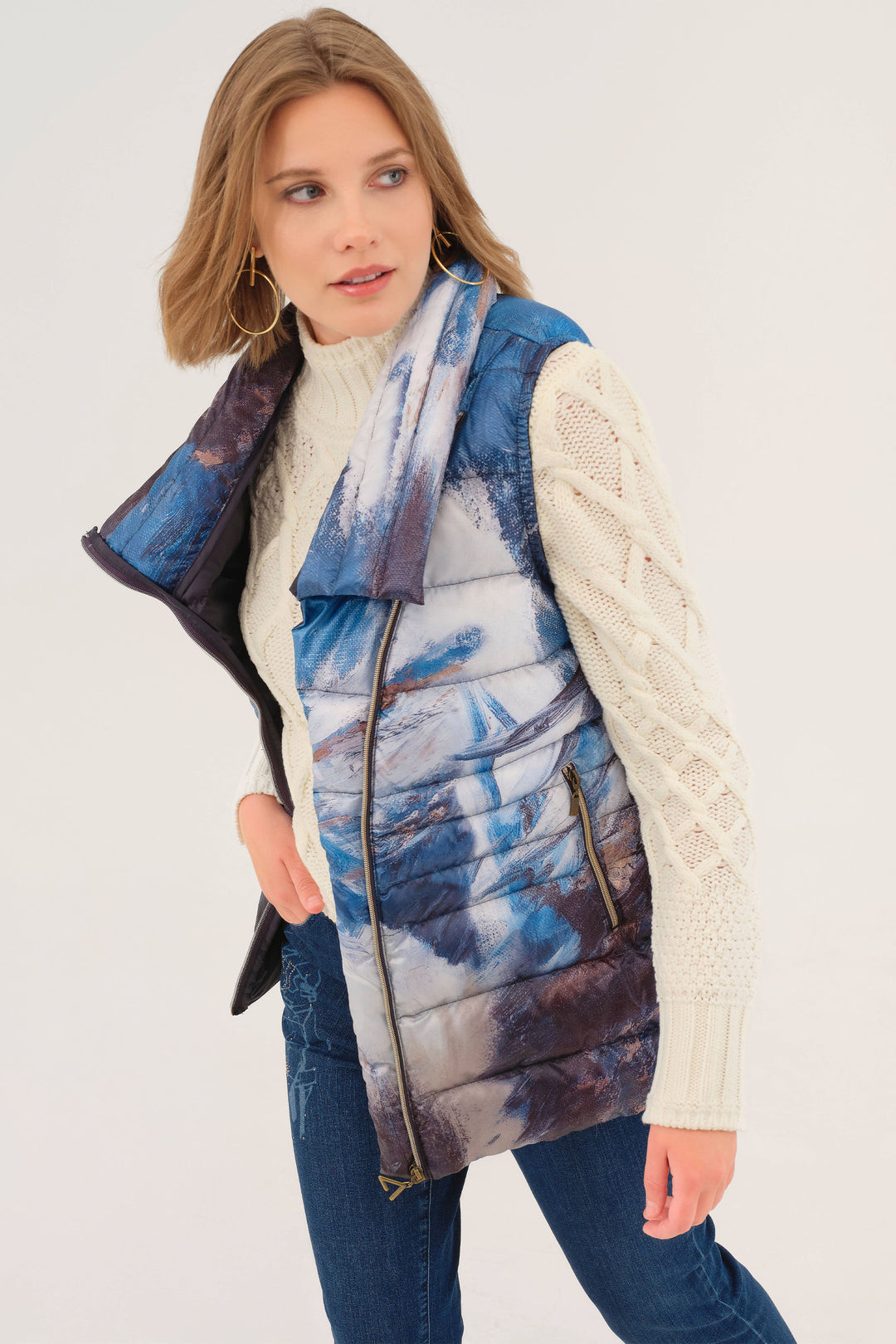 Woman wearing a patterned puffer vest over a white sweater on a white background