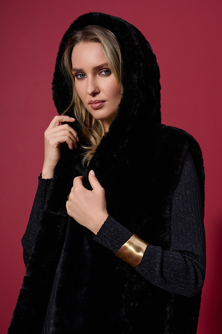 Woman wearing a black hooded faux fur vest with gold cuffs against a red background