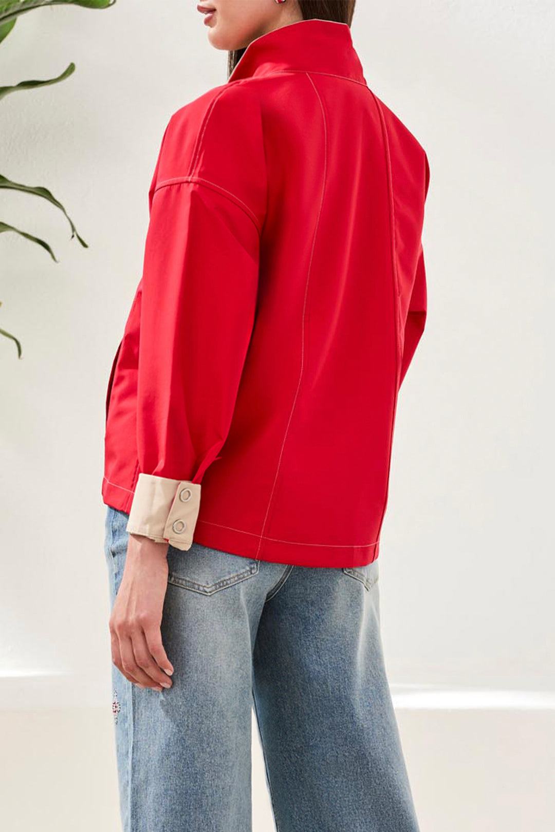 Person wearing a red jacket and light blue jeans against a white background