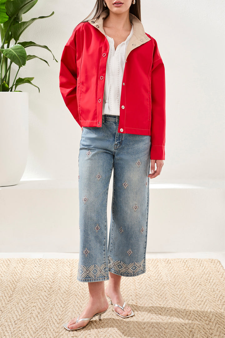 Person wearing a red jacket, white shirt, and blue jeans with a plant in the background