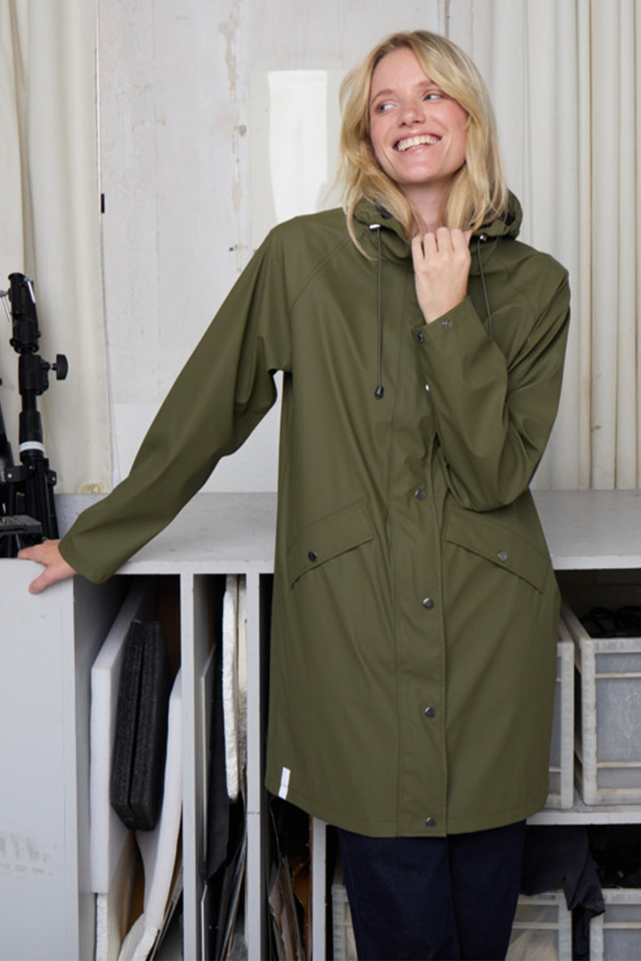 Woman wearing a green raincoat indoors with a white background