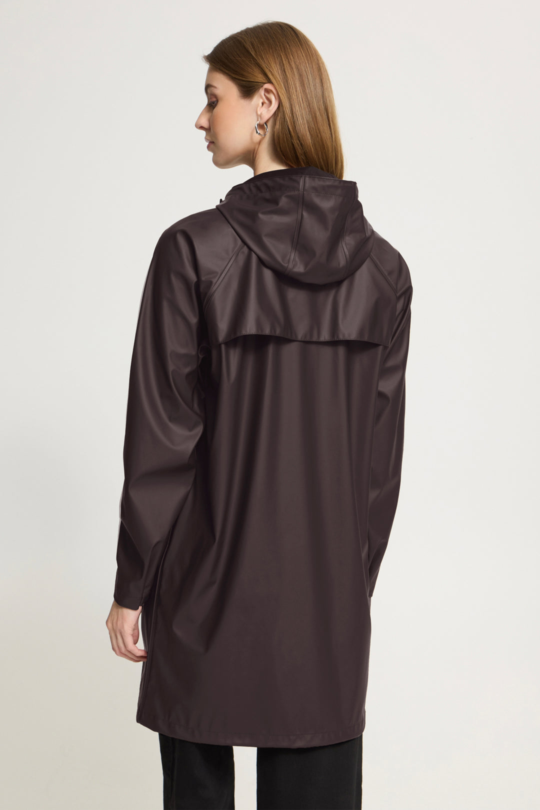 A woman shown from the back wearing a dark brown hooded raincoat against a plain light gray studio background.