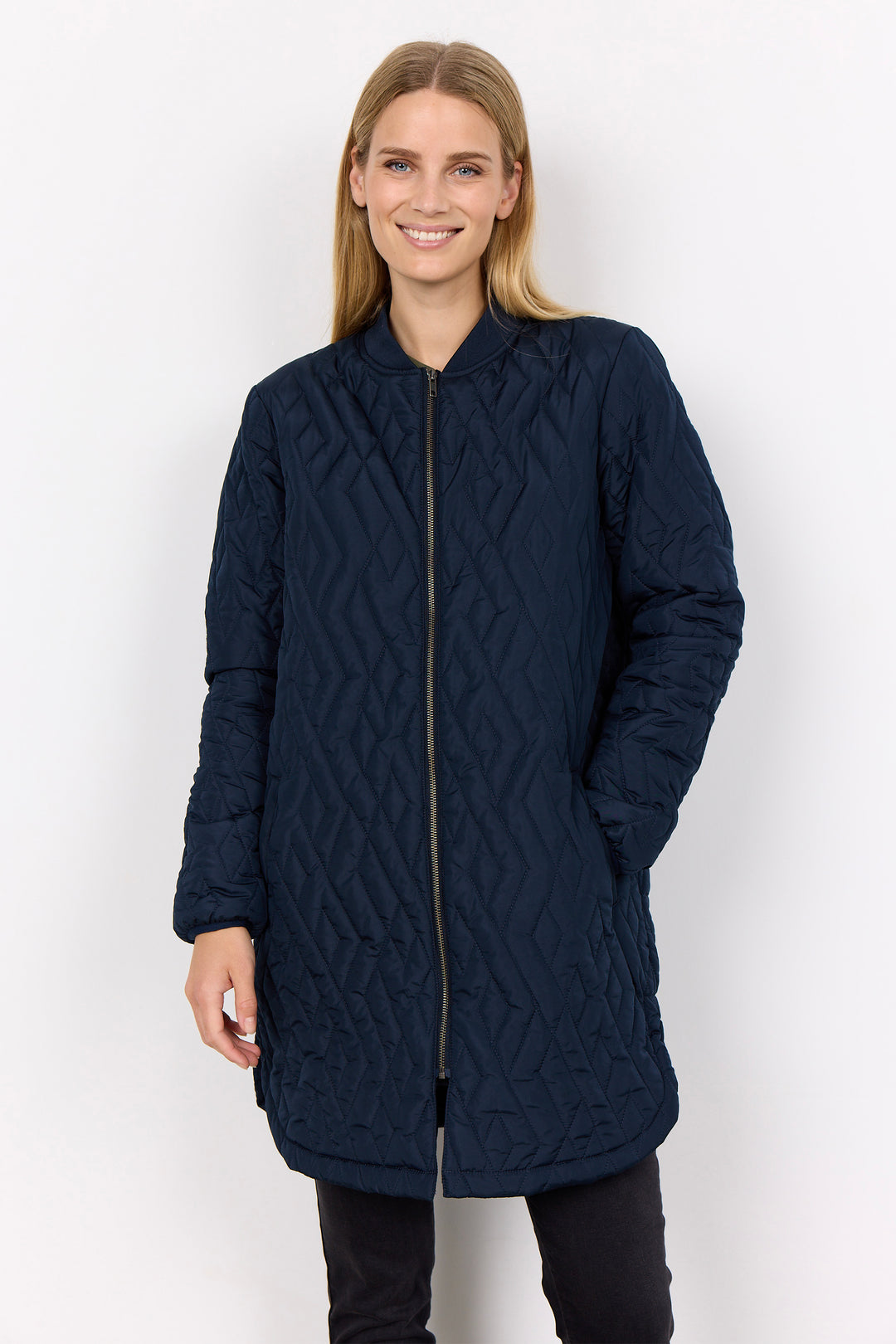 A woman modeling a dark navy blue quilted jacket with a geometric diamond pattern, standing against a plain white studio background.