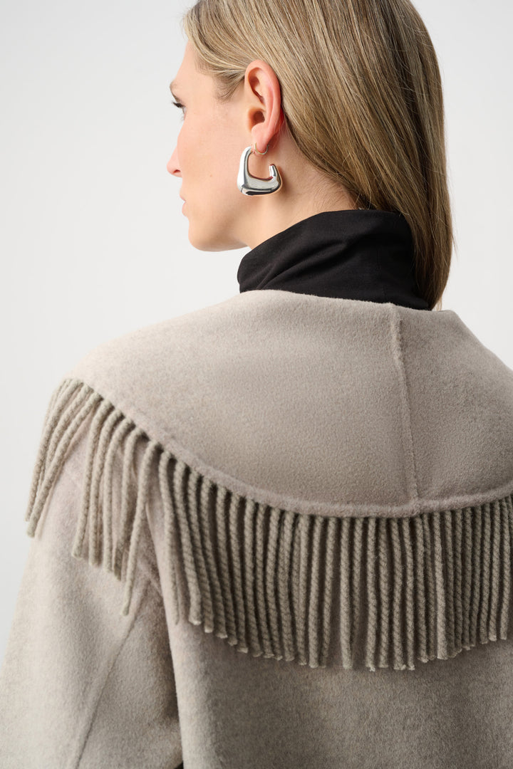 Person wearing a beige fringe jacket on a plain background