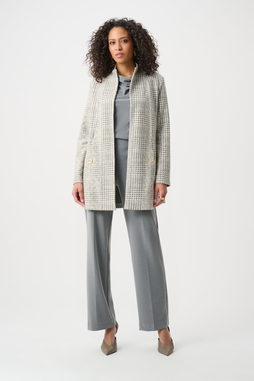 Woman wearing a checkered blazer over a gray top and pants on a white background