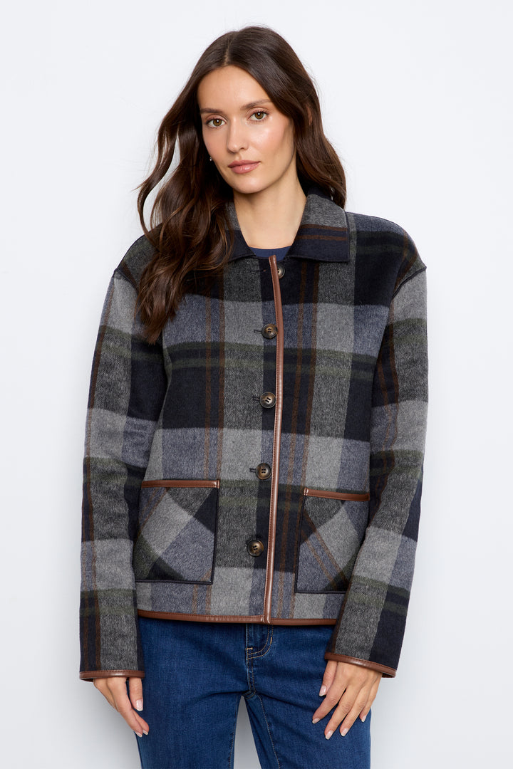 A woman wearing a gray and black plaid button-up jacket with brown trim, paired with blue jeans, against a plain light gray background.