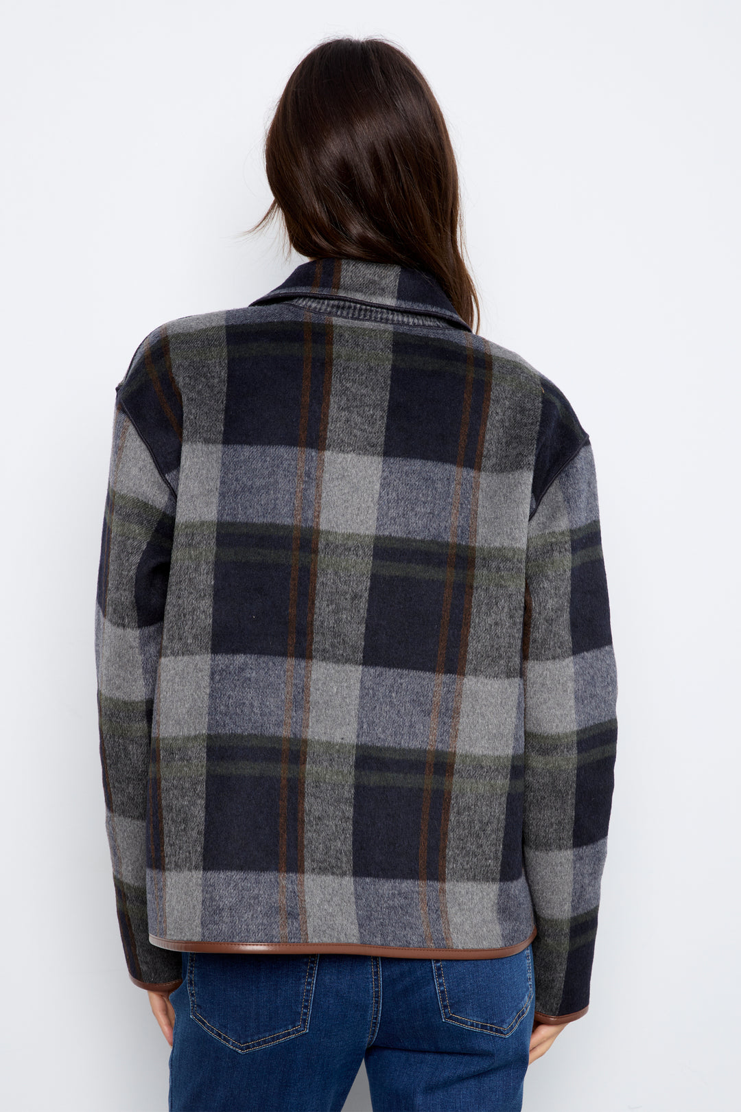 A woman modeling a dark gray and navy plaid textured jacket with brown buttons and brown trim, paired with blue jeans.
