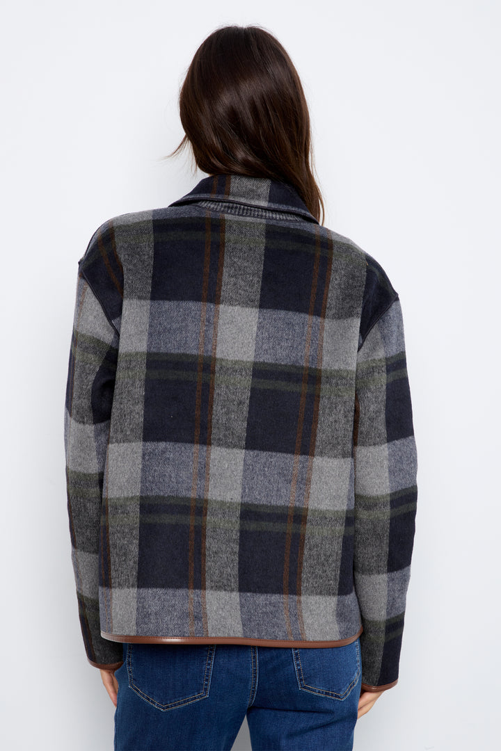 A woman modeling a dark gray and navy plaid textured jacket with brown buttons and brown trim, paired with blue jeans.