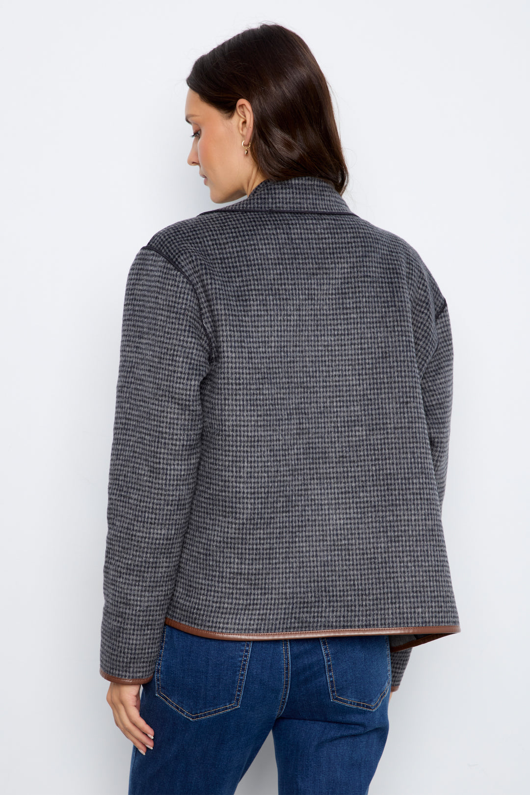 A woman shown from the back wearing a dark gray and black micro-check patterned jacket with brown leather trim, paired with blue jeans, against a plain white background.