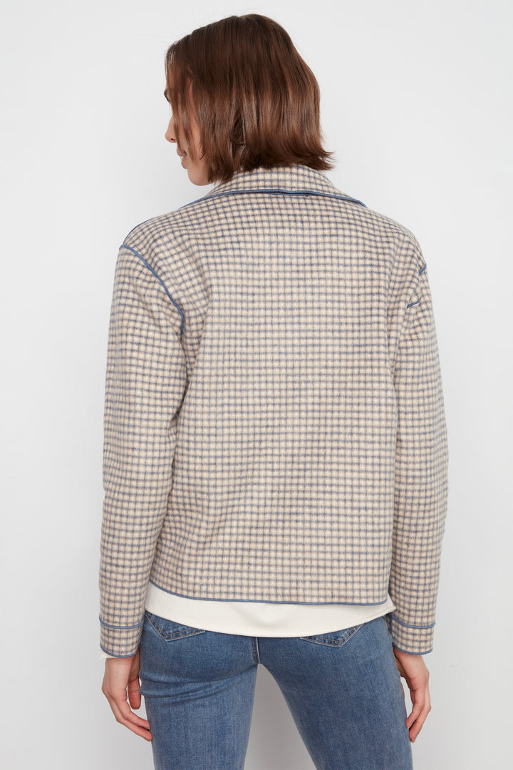 A woman shown from the back wearing a cream-colored plaid jacket with blue and brown stripes, paired with blue jeans, against a plain white background.