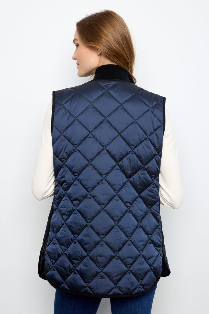A woman shown from the back wearing a navy blue diamond-quilted puffer vest over a cream long-sleeve top and blue jeans, against a plain white studio background.