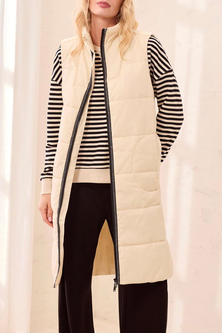 Woman wearing a long cream puffer vest over a striped shirt with a plain background