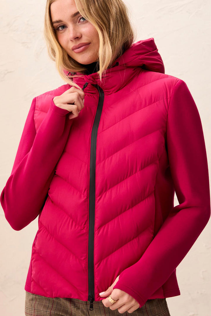 A woman wearing a bright pink hooded puffer vest with a black front zipper, posed against a light beige textured wall.