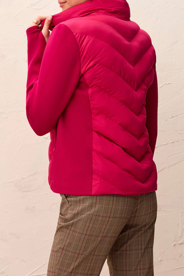 A person wearing a bright pink quilted puffer jacket with a high collar, shown from the back against a textured off-white wall.