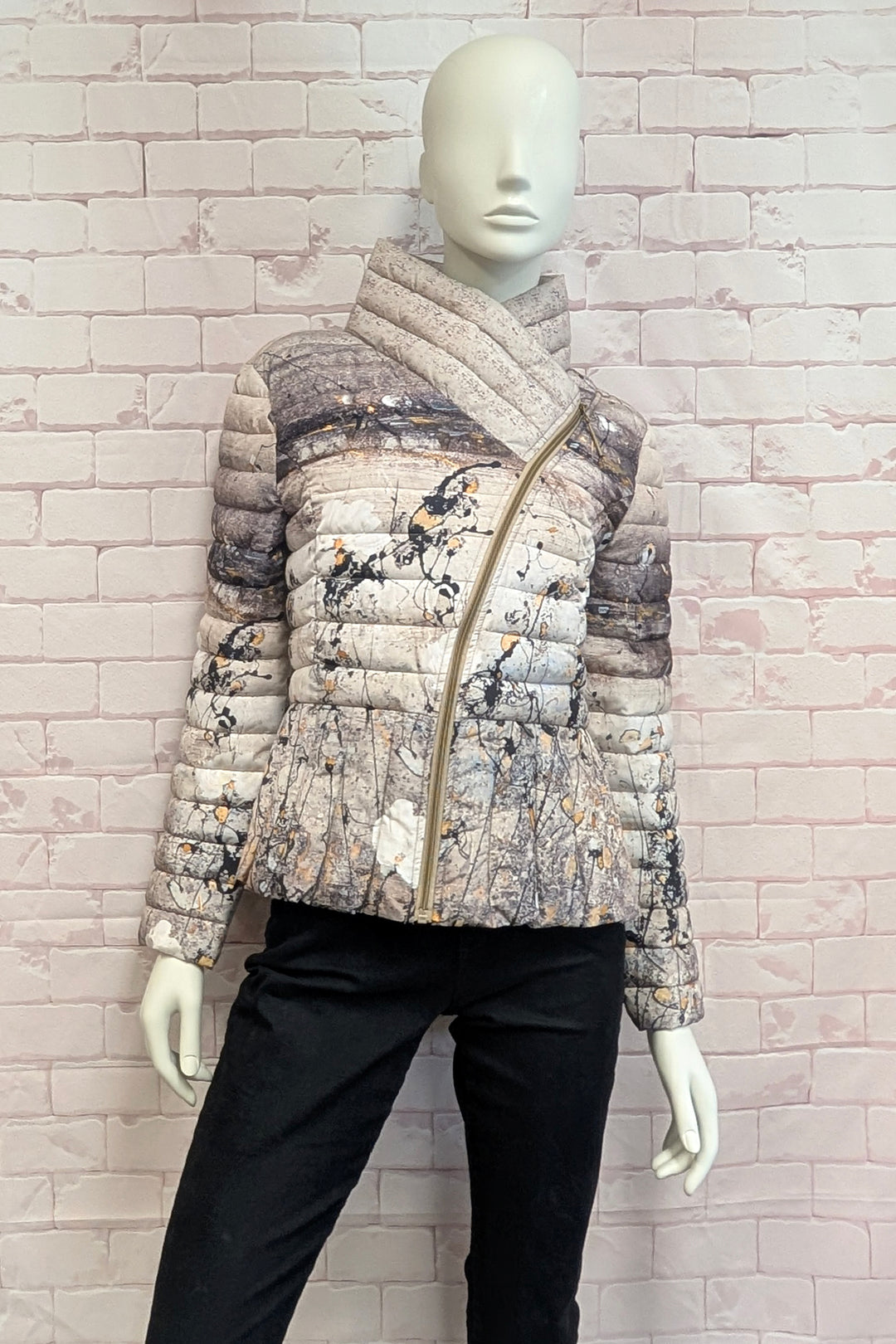 Mannequin wearing a women's quilted puffer jacket featuring an abstract birch tree bark print in shades of gray, white, and beige, with a gold-toned asymmetrical zipper and a high collar.