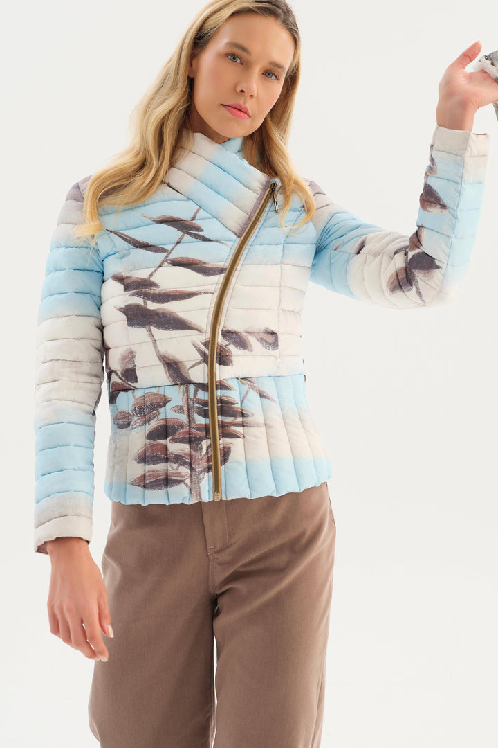 A woman modeling a light blue and white striped quilted jacket with a brown bird print and a gold zipper, paired with brown pants, against a plain white background.