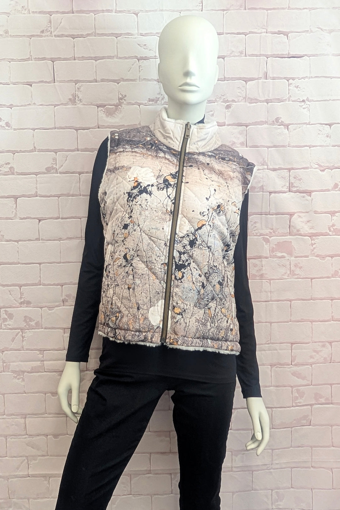 A mannequin modelling a sleeveless zip-front vest with a high stand-up collar, featuring an abstract painterly print in muted gray, beige, brown, and white tones.
