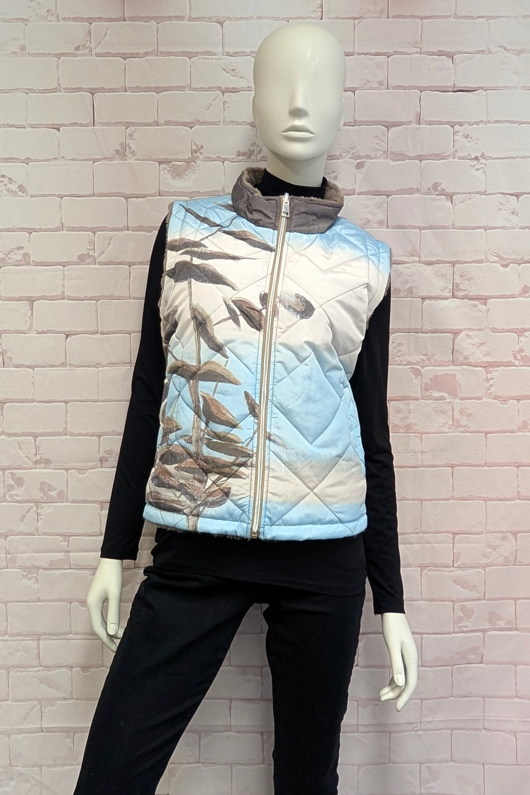 A mannequin wearing a sleeveless quilted vest with a high collar, featuring a light blue and white background with a printed pattern of brown birds perched on branches