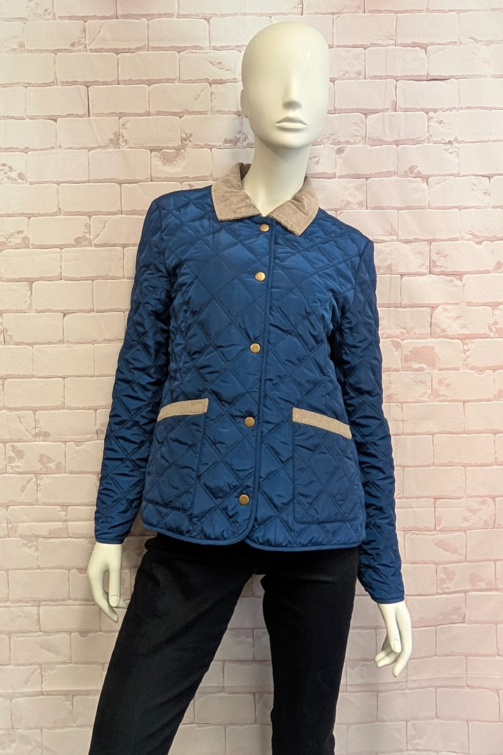 Mannequin wearing a quilted jacket in dark blue with a contrasting beige fleece collar and matching beige trim on the pockets, featuring gold-tone buttons.