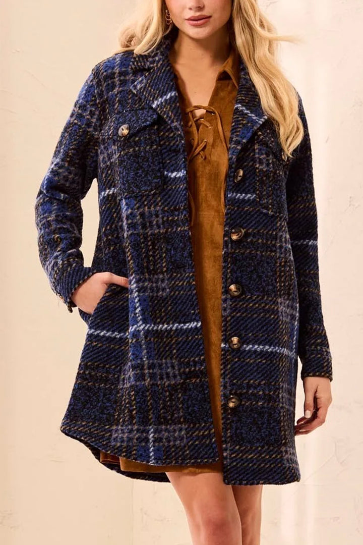 A woman wearing a dark navy plaid coat over a camel coloured dress in front of a beige background