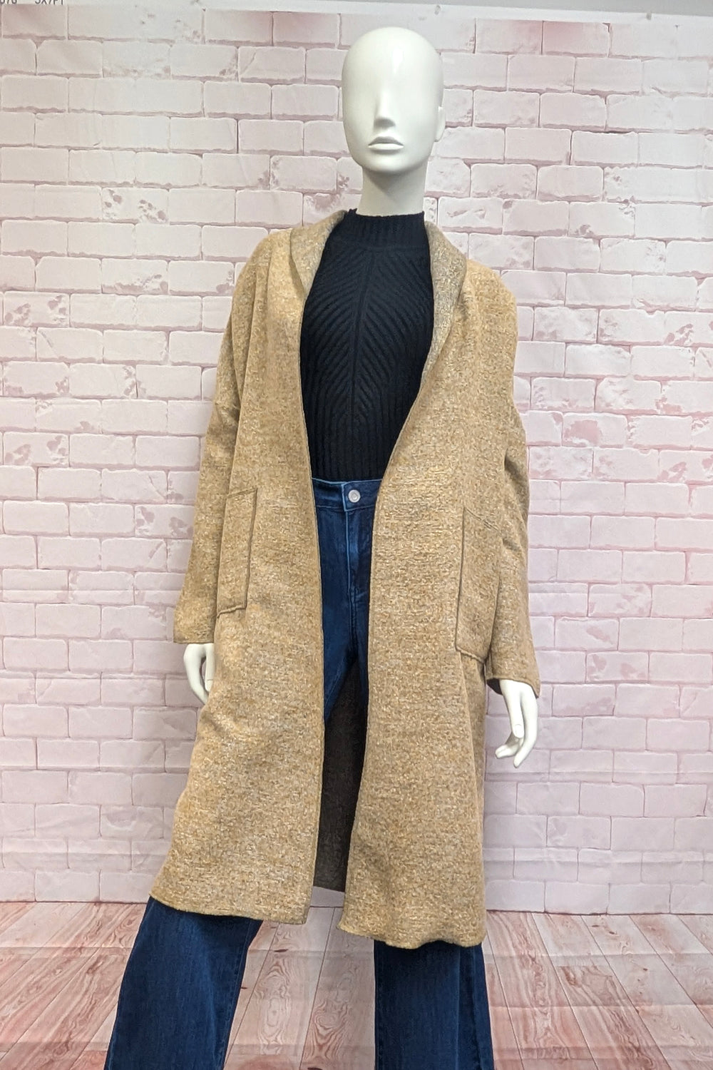 A mannequin modelling a boucle coat in front of a brick background. 