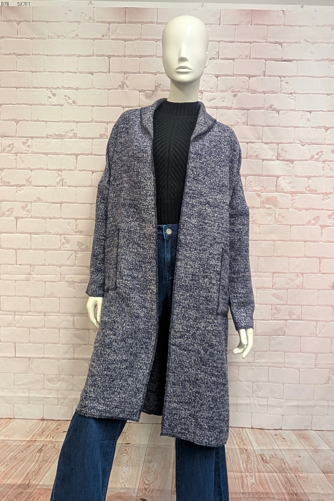 A mannequin modelling a boucle coat in front of a brick background. 
