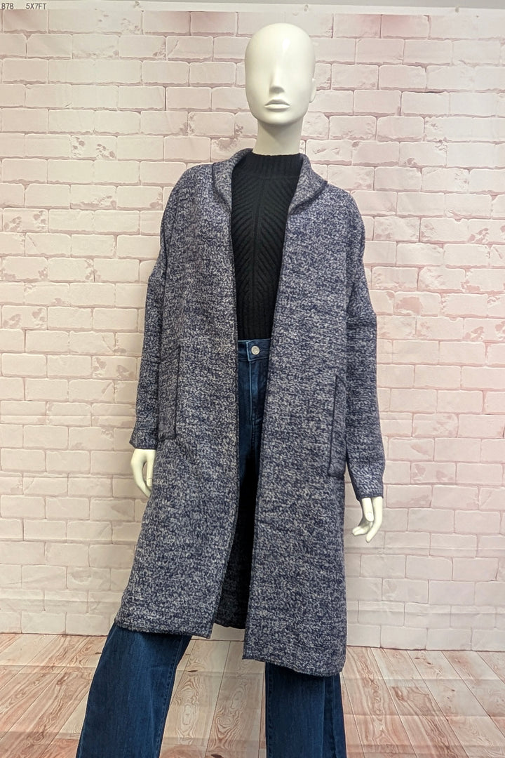 A mannequin modelling a boucle coat in front of a brick background. 
