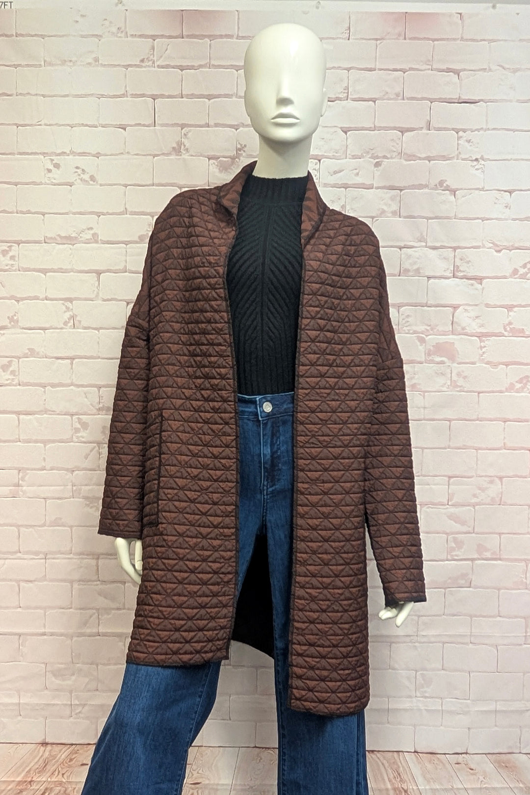 A mannequin modelling a quilted coat in front of a brick background. 