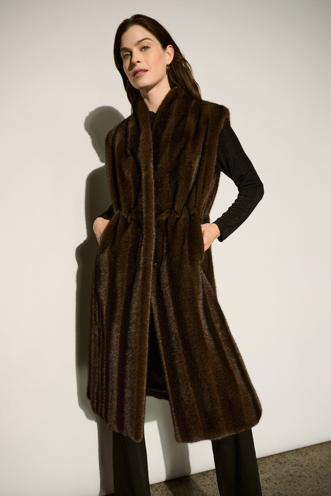 A woman wearing a long brown faux fur vest and black top and pants. 