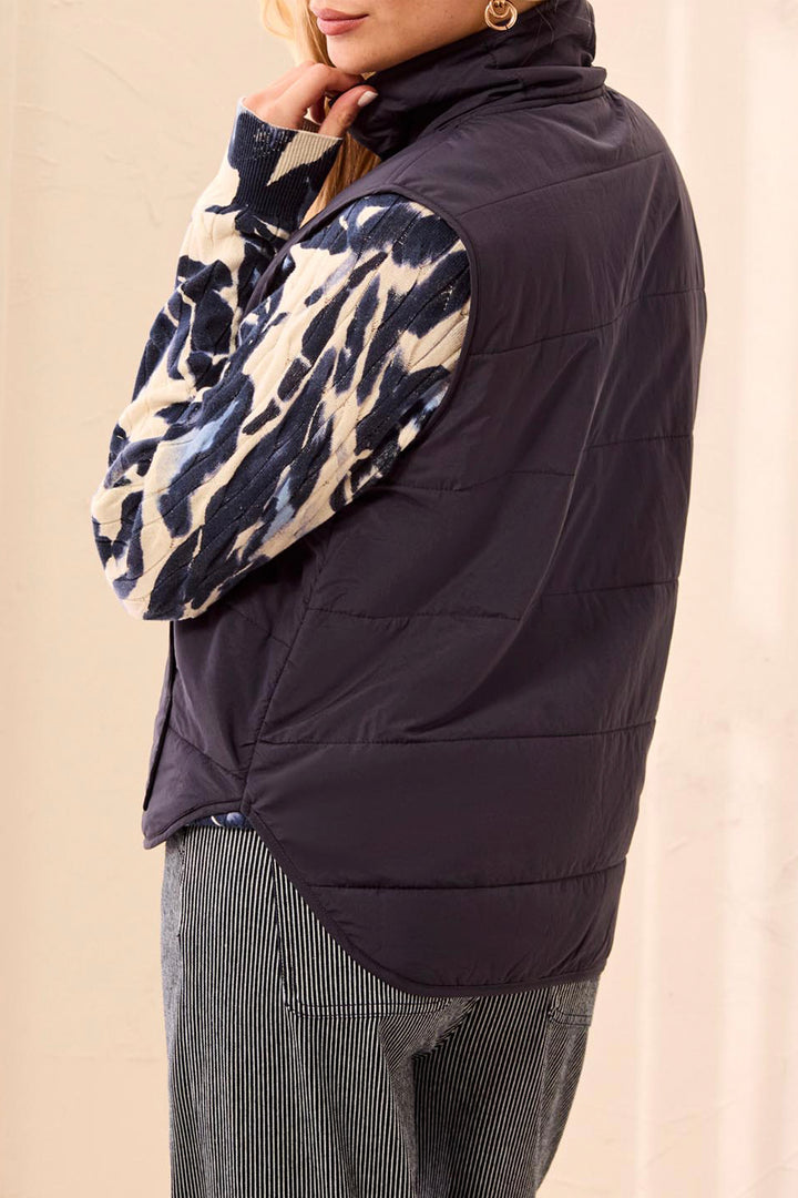 A woman shown from the back modelling a navy puffer vest and sweater standing in front of a light beige background. 