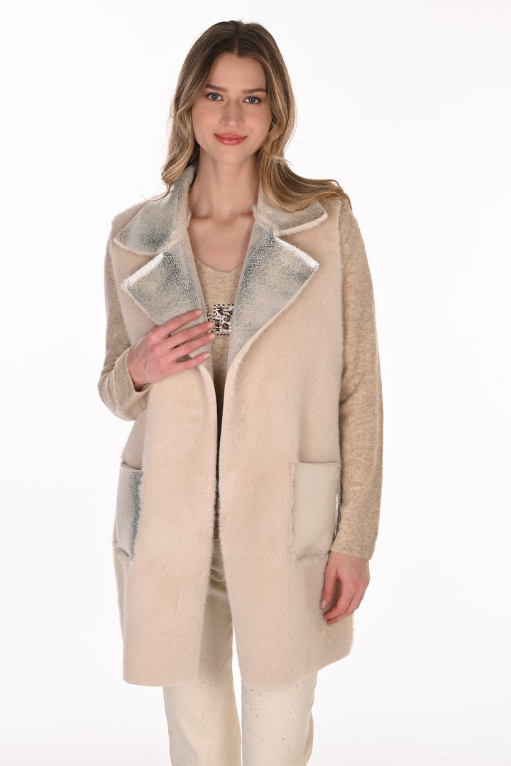 A woman wearing a silver and cream long vest standing in front of a light grey background. 