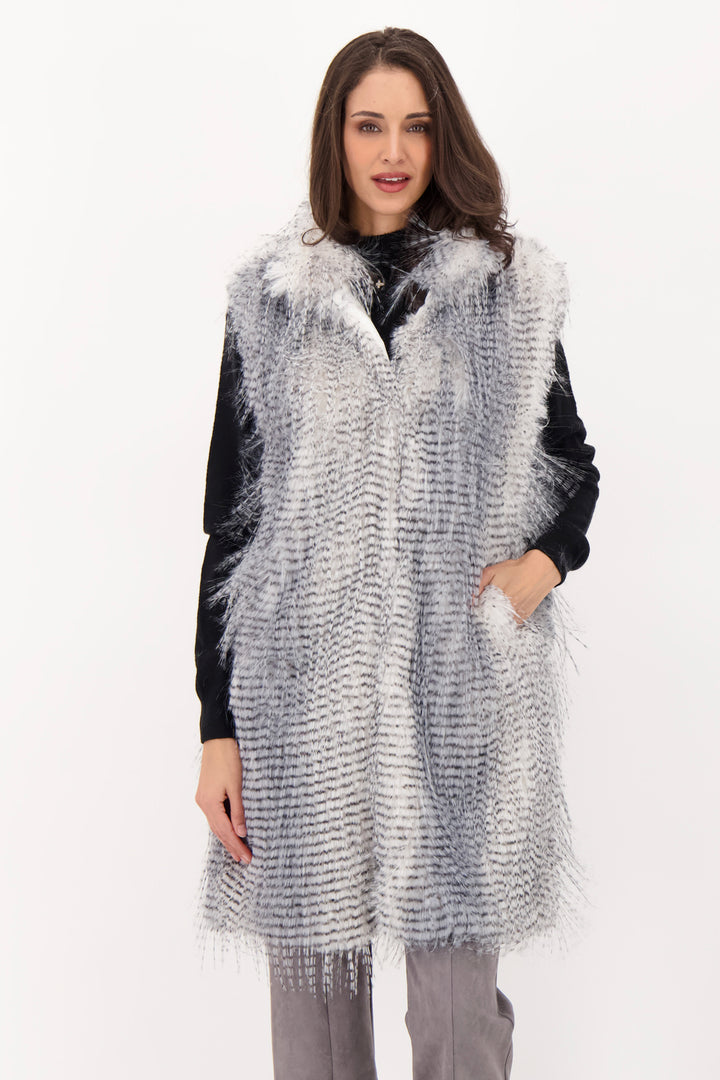 A woman wearing a long grey faux fur vest over a black top and grey jeans. 