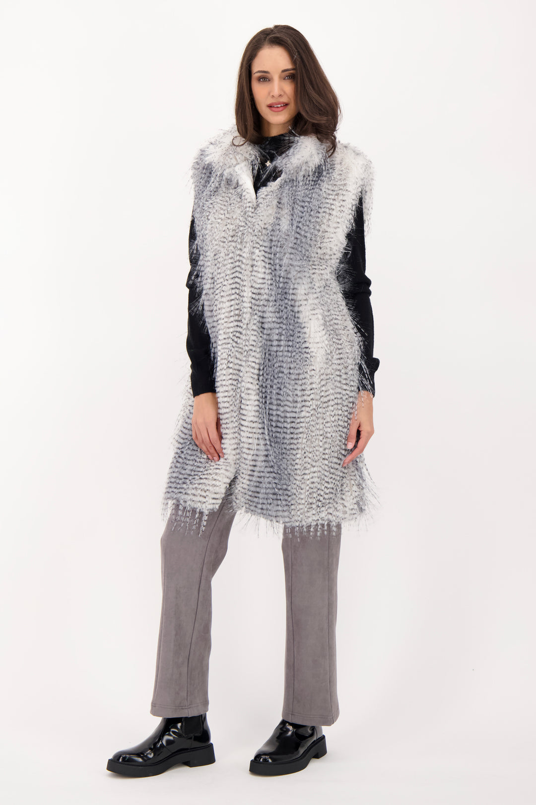 A woman wearing a long grey faux fur vest over a black top and grey jeans. 