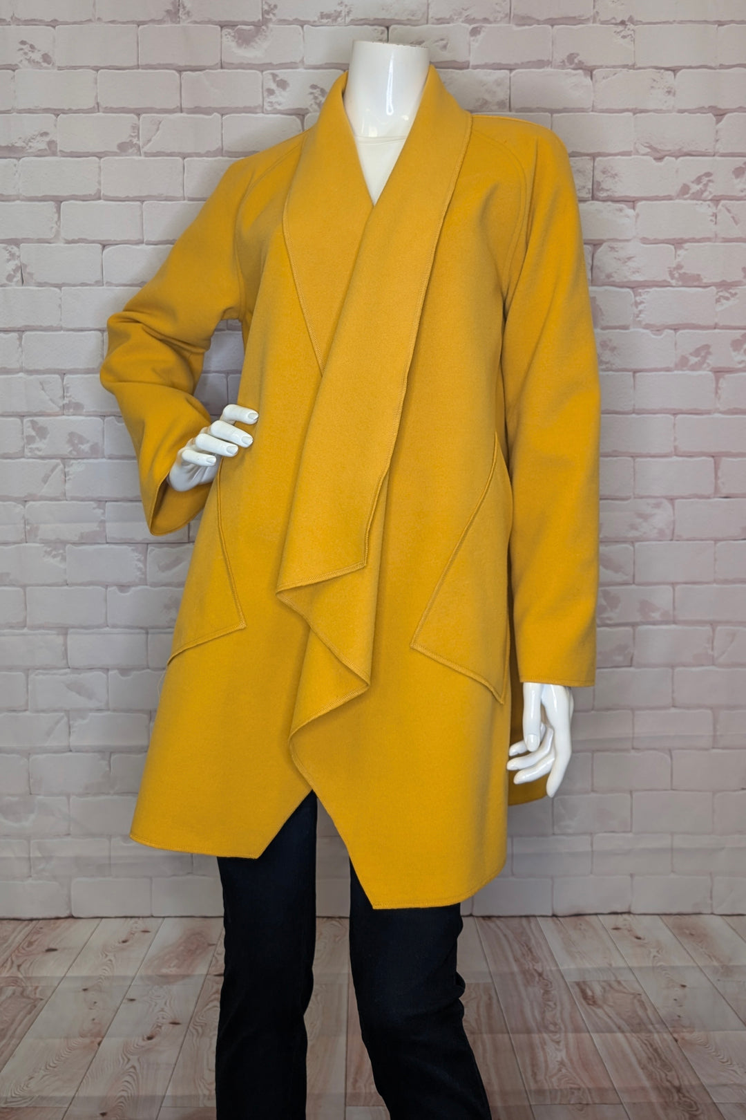 Mustard yellow coat on a mannequin against a brick wall.