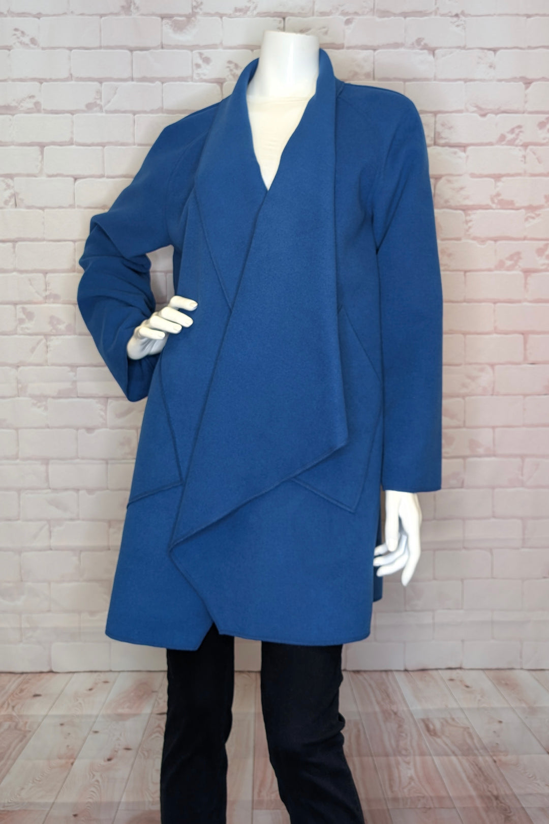 Blue coat on a mannequin against a white brick wall.