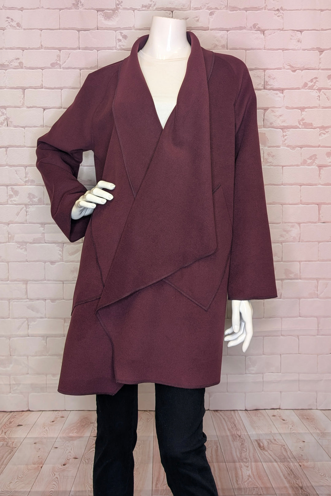 Mannequin wearing a burgundy coat against a brick wall.