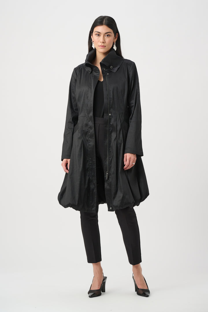 A woman wearing a black dress coat with stand collar, and a balloon hem in front of a white background. 