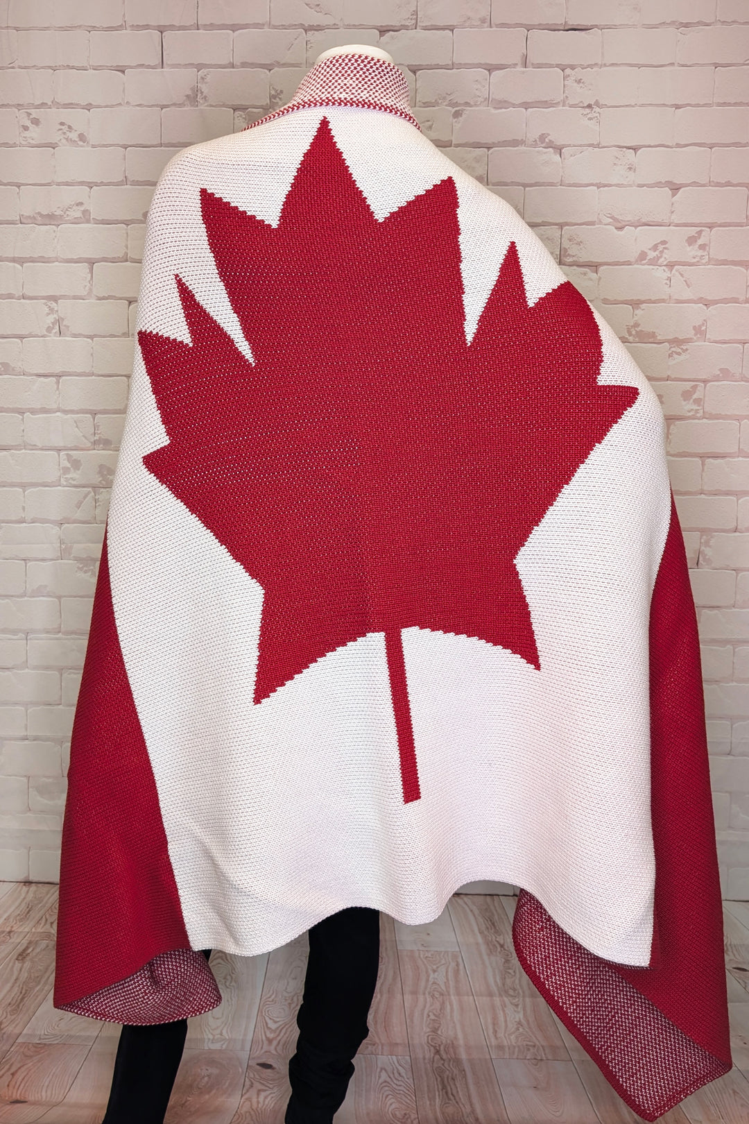 Person wearing a red and white maple leaf patterned blanket against a wooden wall.