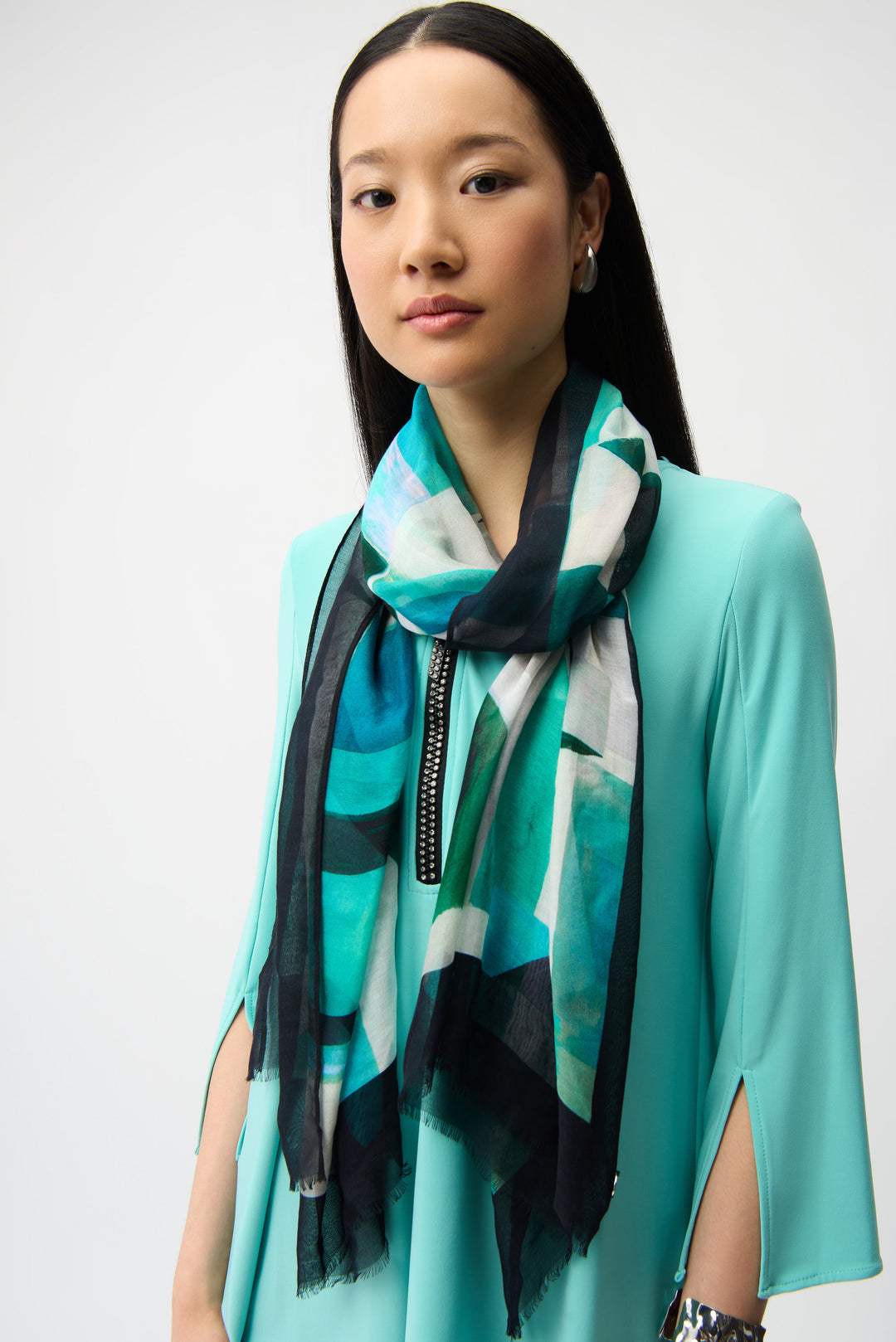 Woman wearing a turquoise scarf with a white and black pattern on a plain background