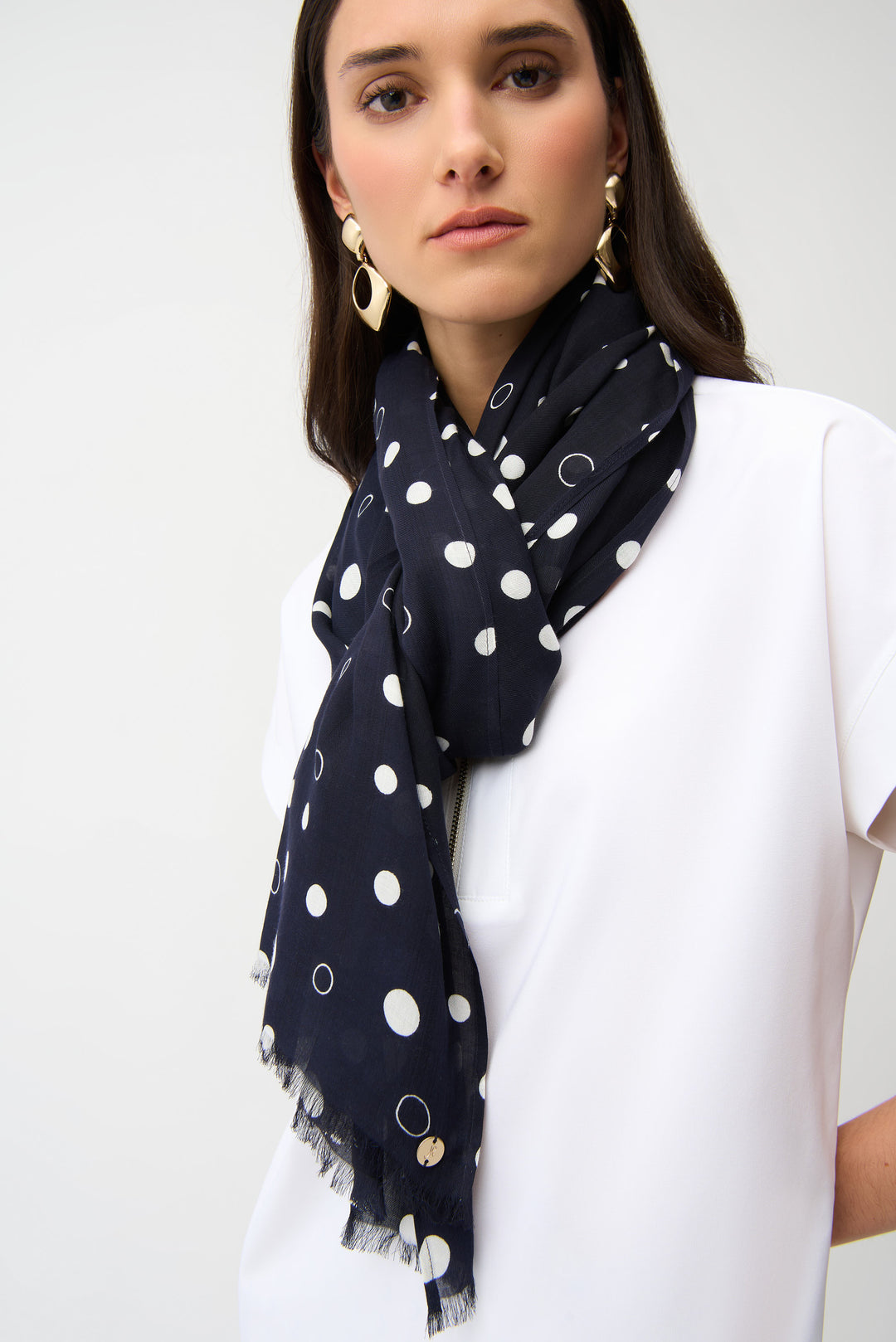 Woman wearing a navy blue scarf with white polka dots on a plain background